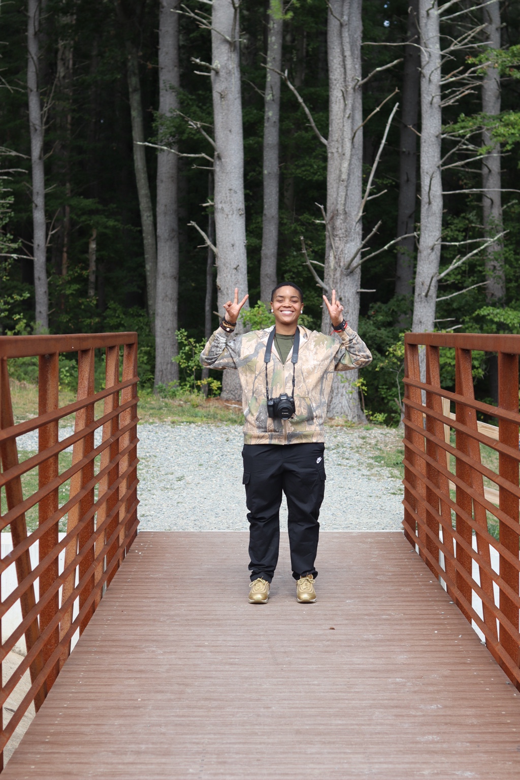 Ty smiling with a camera on a bridge, holding up peace signs